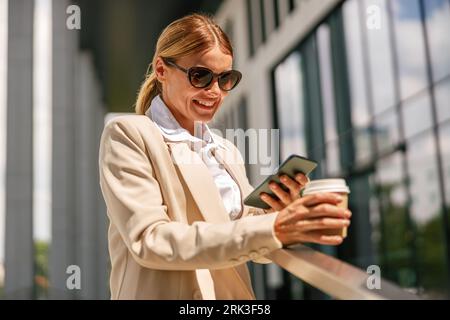 Una donna manager matura sta scattando una tazza di caffè al telefono durante le pause fuori dall'ufficio Foto Stock