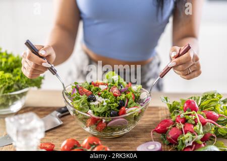 Le mani femminili mescolano una sana insalata primaverile a base di vari ingredienti. Concetto di stile di vita sano. Foto Stock