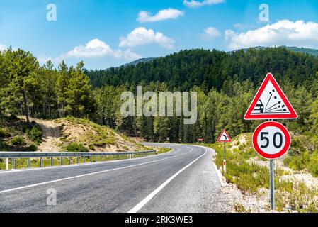 50 km/h speed limit and warning signs on the winding asphalt road going through the forest on the mountain Stock Photo