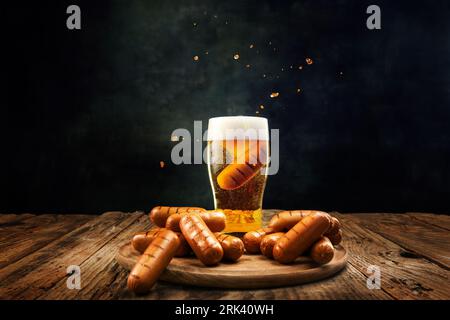 Bicchiere con deliziosa birra lager spumeggiante con salsicce alla griglia su un tavolo di legno su sfondo scuro Foto Stock