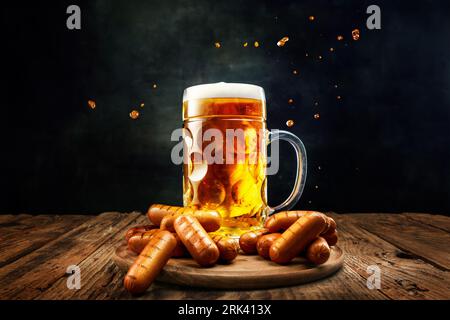 Tazza con deliziosa birra lager fresca con salsicce grigliate come antipasti su un tavolo di legno su sfondo scuro Foto Stock