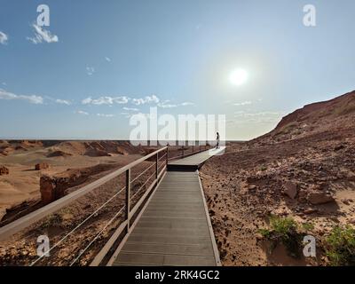 An arid desert trail extends into the horizon, a clear blue sky above it Stock Photo