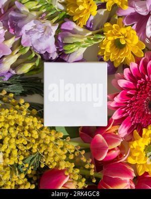 A vertical top view of a blank white box surrounded by colorful flowers Stock Photo