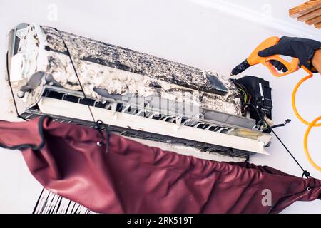 Pulizia del climatizzatore mediante spruzzatura. L'uomo lava via una schiuma speciale per pulire il condizionatore d'aria. Mantenendo il concetto di condizionatore d'aria. Foto Stock