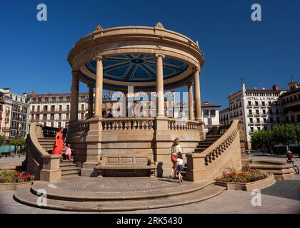 Pamplona, Spagna - 2 agosto 2022: Donna che indossa un abito rosso con la figlia accanto al monumento Padiglione in Piazza del castello nella città vecchia di Foto Stock