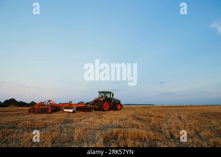 Il trattore moderno con un erpice pesante a dischi trainati lavora su un ampio terreno collinare. Campagna agricola autunnale o primaverile Foto Stock