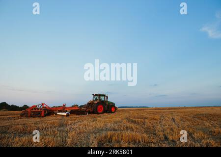 Il trattore moderno con un erpice pesante a dischi trainati lavora su un ampio terreno collinare. Campagna agricola autunnale o primaverile Foto Stock