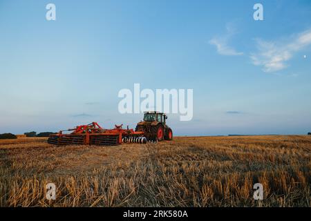 Il trattore moderno con un erpice pesante a dischi trainati lavora su un ampio terreno collinare. Campagna agricola autunnale o primaverile Foto Stock