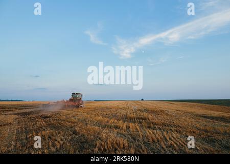 Il trattore moderno con un erpice pesante a dischi trainati lavora su un ampio terreno collinare. Campagna agricola autunnale o primaverile Foto Stock