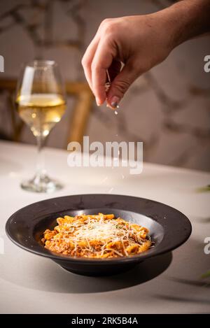 Una persona cosparge di formaggio su un recipiente di pasta deliziosa con carne e salsa Foto Stock