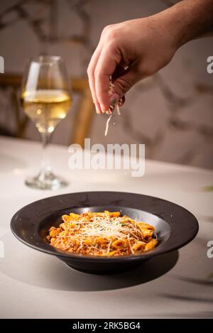 Una persona cosparge di formaggio su un recipiente di pasta deliziosa con carne e salsa Foto Stock