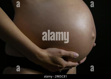 Una bella donna incinta che tiene la pancia sullo sfondo nero Foto Stock