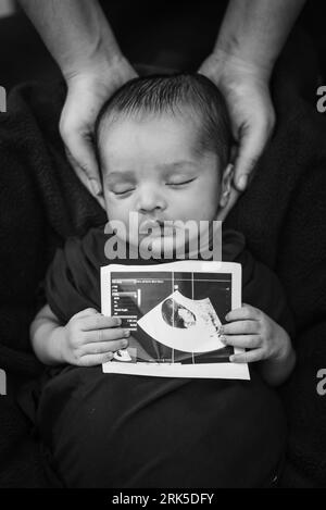 neonato che tiene in mano una copia ecografica e dorme al palmo della madre in bianco e nero Foto Stock