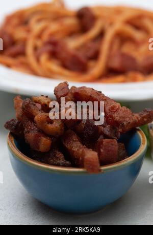 Bucatini fatti in casa all'Amatriciana, guance di manzo cotte su pasta, formaggio e salsa di pomodoro in un recipiente bianco Foto Stock