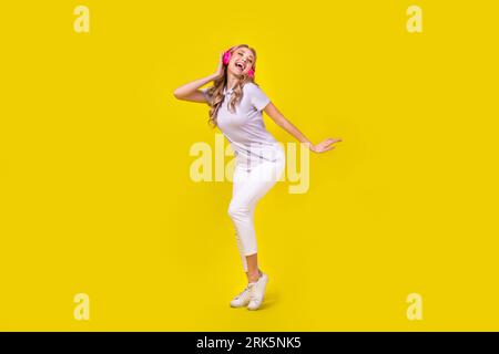 Full size photo of lovely nice girl wear violet polo white trousers sing pop song in headphones isolated on yellow color background Stock Photo