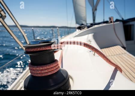 Un primo piano del verricello sul ponte di uno yacht, con la barca a vela sullo sfondo Foto Stock