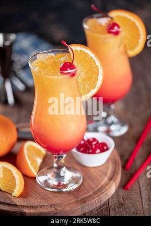 Cocktail tequila all'alba con fetta di ciliegia e arancia su un tavolo rustico in legno Foto Stock