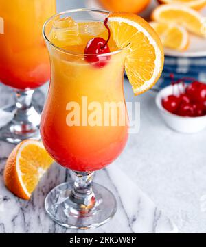 Cocktail tequila all'alba con fetta di ciliegia e arancia su un tavolo di marmo Foto Stock