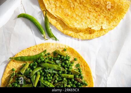 Two flour tortillas filled with fresh green peas and beans, placed on a white paper background Stock Photo