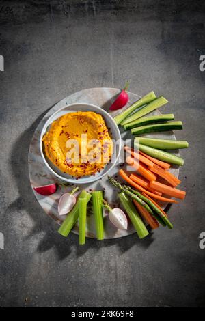 Un vassoio da portata bianco rotondo con un assortimento colorato di verdure come carote, sedano e ravanelli disposti intorno a una ciotola di salsa cremosa all'hummus Foto Stock