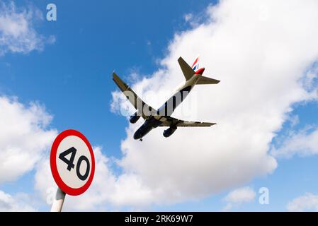 Aereo di linea in fase finale per atterrare all'aeroporto di Londra Heathrow, Regno Unito, superando un cartello stradale di 40 km/h sulla A30. limite di velocità di 40 miglia all'ora Foto Stock