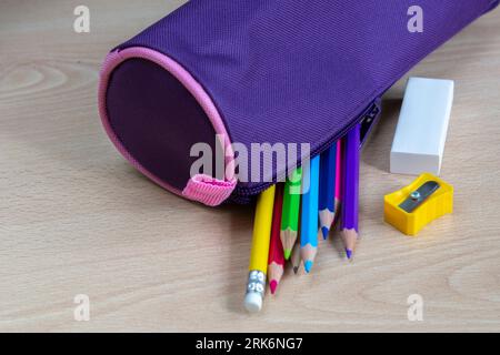 purple pencil case with colored paints and other school supplies on light wooden desk Stock Photo