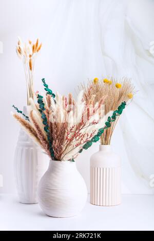 Three decorative vases featuring natural greenery and colorful flowers, arranged in a modern, eye-catching display Stock Photo