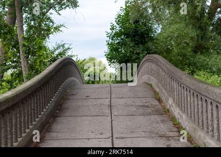Un ponte di pietra sopra un canale che conduce ai lussureggianti alberi verdi Foto Stock