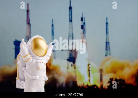 Un astronauta giocattolo si trova sullo sfondo di un razzo che decolla da una rampa di lancio. Foto Stock