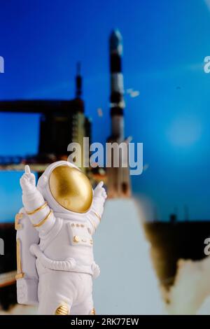 Un astronauta giocattolo si trova sullo sfondo di un razzo che decolla da una rampa di lancio. Foto Stock