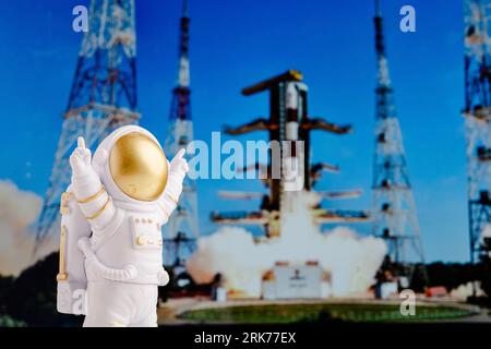 Un astronauta giocattolo si trova sullo sfondo di un razzo che decolla da una rampa di lancio. Foto Stock