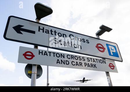 La stazione di Hatton Cross firma con un aereo di linea in finale per atterrare all'aeroporto di Londra Heathrow, Regno Unito. Stazione di Hatton Cross e parcheggio Foto Stock