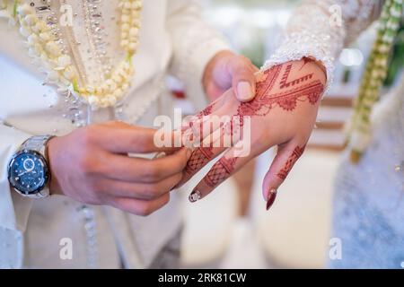 Un marito e una moglie hanno messo i rispettivi fedi nuziali in una tradizionale cerimonia di nozze indonesiana. Lo sposo mette un anello al dito della sua amata moglie. TH Foto Stock