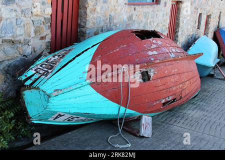 Una barca di legno intemprata siede abbandonata su un marciapiede della città Foto Stock