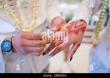 Un marito e una moglie hanno messo i rispettivi fedi nuziali in una tradizionale cerimonia di nozze indonesiana. Lo sposo mette un anello al dito della sua amata moglie. TH Foto Stock