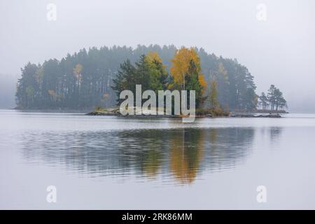 A small island located in the middle of a tranquil lake, surrounded by lush greenery. Foto Stock