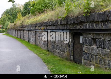A rural road featuring an old wall with lush green grass growing across its surface. Stock Photo