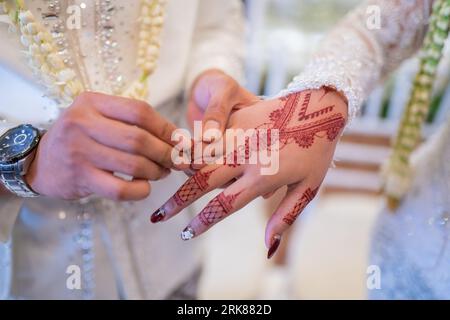 Un marito e una moglie hanno messo i rispettivi fedi nuziali in una tradizionale cerimonia di nozze indonesiana. Lo sposo mette un anello al dito della sua amata moglie. TH Foto Stock