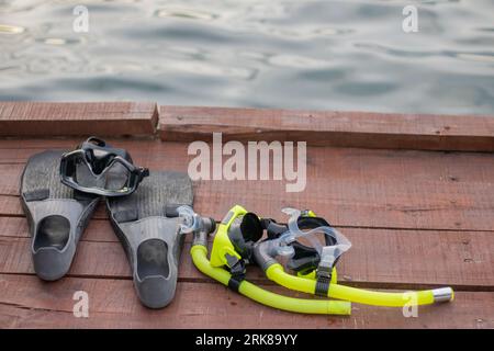 Set completo di attrezzature per immersioni subacquee con attenzione selettiva al molo di legno. Alette, misuratore di profondità, regolatore bilanciato, generatore di gas, maschera da immersione e snorkeling. Foto Stock