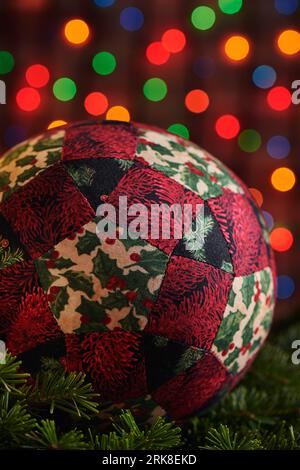 Palla decorativa natalizia cucita da pezzi di tessuti su rami di abete rosso, sfondo bokeh dai colori scuri Foto Stock
