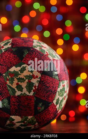 Palla decorativa natalizia cucita con pezzi di tessuti su sfondo bokeh scuro e colorato Foto Stock