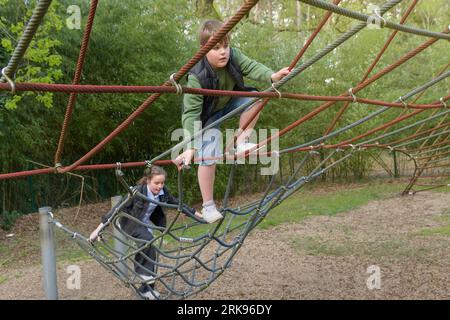 Ragazzo e ragazza adolescente che si arrampicano sulla ragnatela con espressione nel parco pubblico. Giorno di sole primaverile Foto Stock