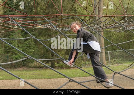 Ragazza adolescente. guardando la telecamera, salendo sulla ragnatela con espressione nel parco pubblico Foto Stock