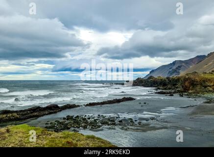 Una Rocky Beach con Bergs sull'Islanda con forti venti e potenti surfisti Foto Stock