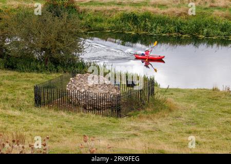 Un canoista filtra lungo il fiume Nene oltre il solo blocco di muratura rimasto seduto sul sito del castello di Fotheringhay che fu smantellato nel 1628. Lo storico castello è stato parte di due momenti importanti della storia inglese. Re Riccardo III nacque a Fotheringhay nell'ottobre 1452. Maria regina di Scozia fu tenuta prigioniera e giustiziata a Fotheringhay nel febbraio 1587. Le pietre rimanenti si trovano accanto al fiume Nene nella contea del Northamptonshire. Foto Stock