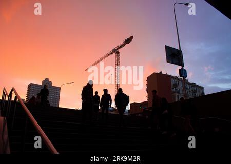 : Un tranquillo tramonto dopo la pioggia dipinge la città con sfumature dorate. I pendolari dalla silhouette scendono in metropolitana sullo sfondo dell'iconico sovietico di Arbat Foto Stock