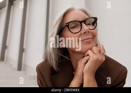 60 anni, donna d'affari dai capelli grigi, ben curata e vestita con stile, gode della libertà durante una pausa dal lavoro Foto Stock