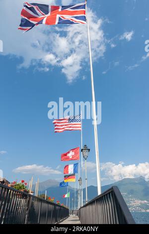 Fila di bastoni di bandiera con bandiere di paesi europei e di altri paesi che volano in brezza Menaggio, Italia, sulle rive del Lago di Como. Foto Stock