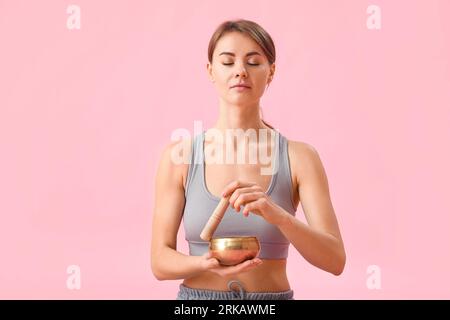 Giovane donna con coppa tibetana di canto meditando su sfondo rosa Foto Stock