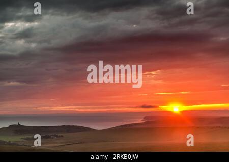 Beachy Head, Eastbourne, Sussex, Regno Unito. 24 agosto 2023. Breve scorcio del tramonto sotto le nuvole tempestose mentre la nebbia marina si muove. Foto scattata dall'area di Beachy Head che guarda a ovest sulle scogliere di Birling Gap e Seven Sisters. Faro di Belle Tout a sinistra della foto. Credito: David Burr/Alamy Live News Foto Stock